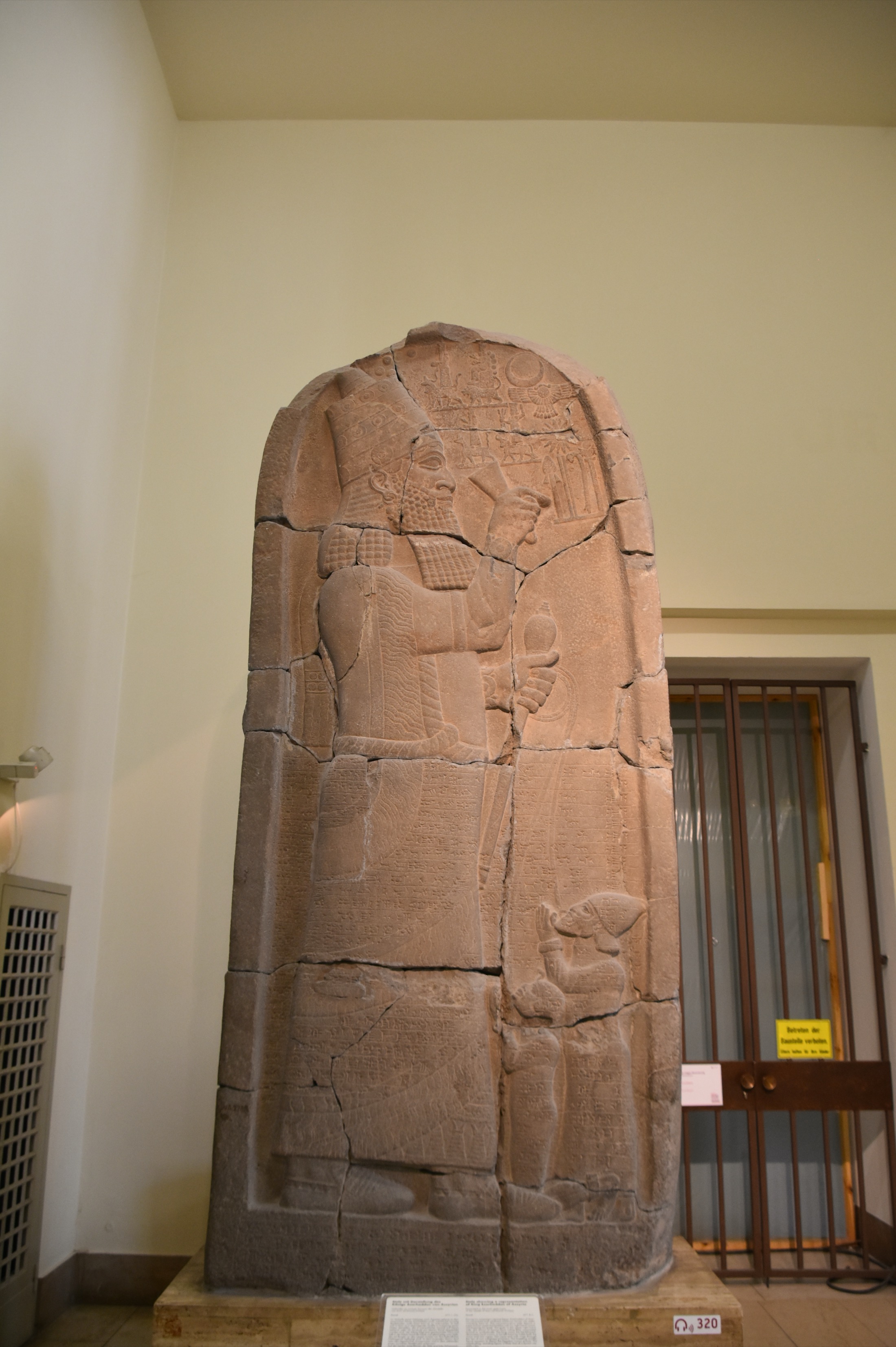 Basalt victory stele of the Assyrian king Esarhaddon, showing him holding a mace and a rope looped through the lips of two kneeling captive figures, with cuneiform inscription covering the surface